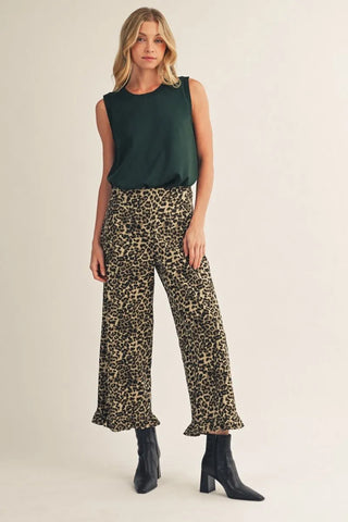 Woman wearing a green sleeveless top and leopard print pants on a beige background