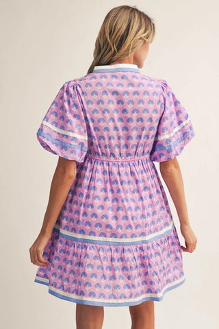 Woman wearing a pink dress with blue patterns on a plain background