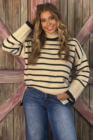Woman wearing a striped sweater and jeans standing against a wooden background