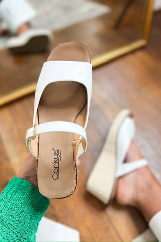 White sandals with a visible brand logo on a wooden floor.