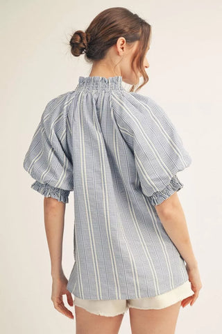 Woman wearing a blue and white striped blouse with puffed sleeves on a beige background