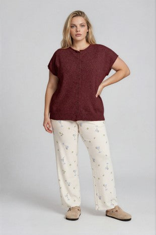 Woman wearing a burgundy top and white pants with a pattern on a plain background