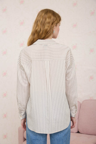 Person wearing a striped shirt standing in front of a pink couch with a patterned wall in the background.