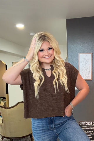Woman posing in a clothing store with a checkered floor and shelves in the background.