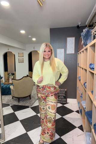 Woman in a bright yellow top and patterned pants standing in a room with checkered floor and shelves.