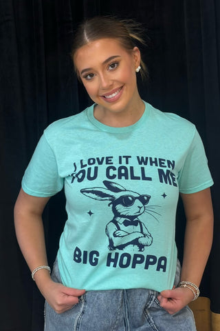 Woman wearing a light blue t-shirt with a graphic and text, standing against a dark background