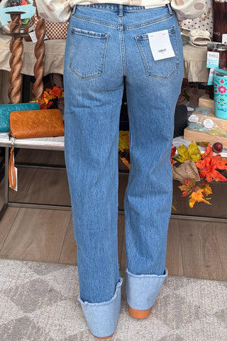 A person shown from the back wearing light blue straight-leg jeans with rolled cuffs, standing in a retail store interior.