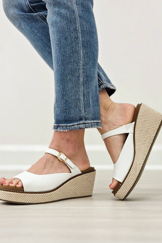 White wedge sandals with brown soles worn with blue jeans on a light background