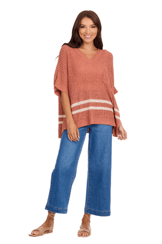 Woman wearing a rust-colored poncho with white stripes and blue jeans on a white background