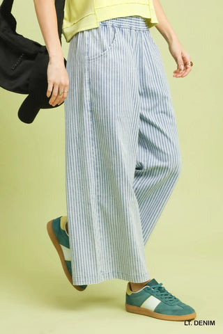 Person wearing blue and white striped wide-leg pants with green sneakers on a light yellow background