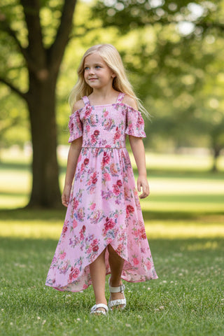 Young girl in a pink floral dress standing on grass with trees in the background