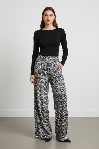 Woman wearing a black long-sleeve top and patterned pants on a plain background