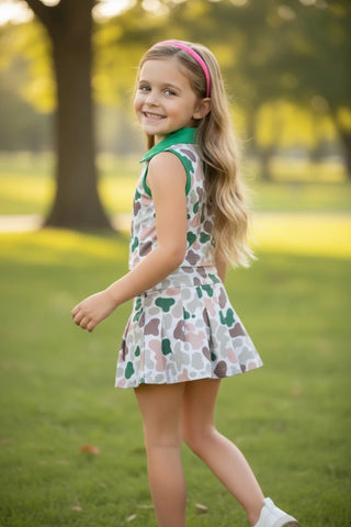 Young girl in a patterned dress standing on grass with trees in the background
