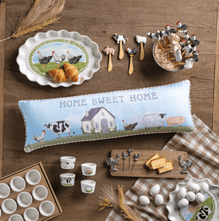Collection of farm-themed kitchen items including a pillow, plates, and utensils on a wooden surface.