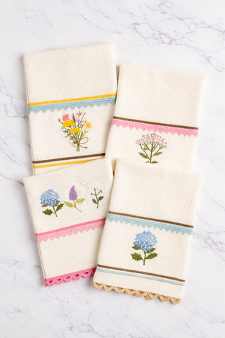 Set of four embroidered towels with floral designs on a white marble surface