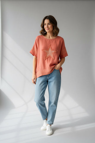 Woman wearing a coral t-shirt with a star design and blue jeans on a white background