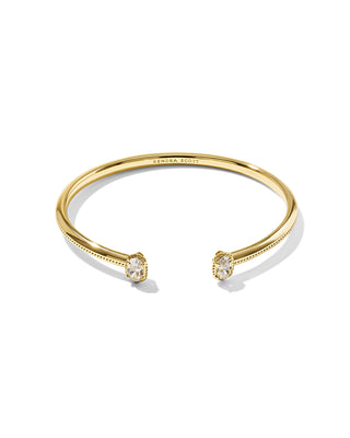 A gold open cuff bracelet with two bezel-set oval clear gemstones, shown on a clean white background. The brand name 'KENDRA SCOTT' is engraved inside the band.