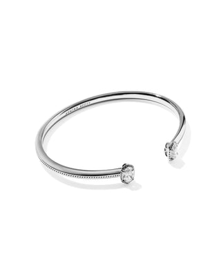 A polished silver-tone open cuff bangle bracelet with two bezel-set clear gemstones, photographed on a clean white background.