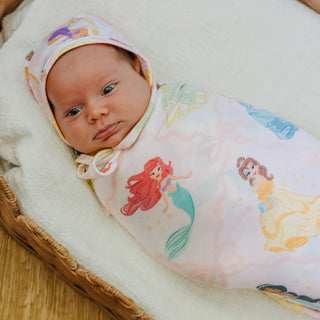 Baby wrapped in a swaddle with mermaid designs, wearing a matching headband.