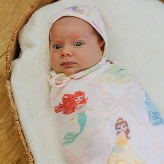 Newborn baby wrapped in a swaddle with mermaid designs, lying on a white cushion.