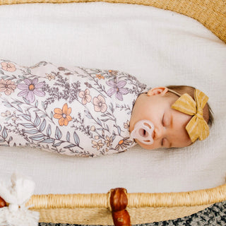 Baby swaddled in a floral blanket with a yellow bow, lying in a woven basket.