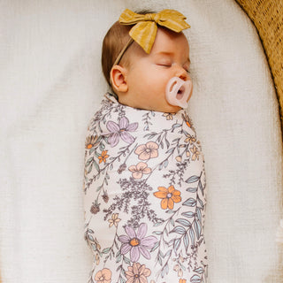 Newborn baby swaddled in a floral blanket with a yellow bow and pacifier.