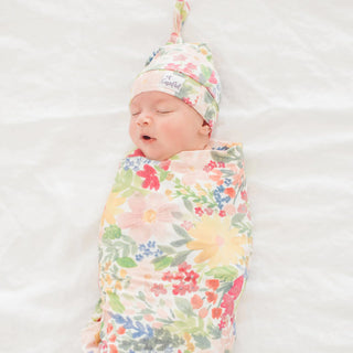 Newborn baby swaddled in a floral blanket with a matching hat on a white background