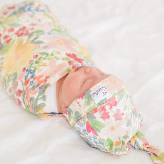 Baby wrapped in a floral swaddle with a visible brand label on a white background