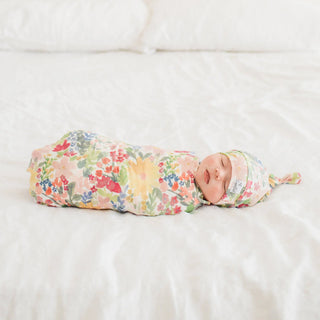 Baby swaddled in a floral blanket and hat on a white surface