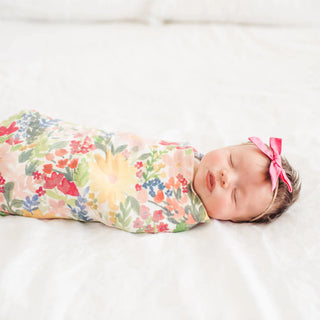 Newborn baby swaddled in a floral blanket with a pink bow on a white background