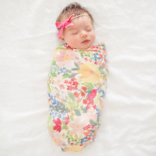 Newborn baby swaddled in a floral blanket with a pink bow on a white background