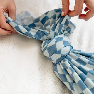 Blue and white checkered fabric being tied into a knot on a light background