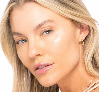 Close-up of a woman with blonde hair and blue eyes wearing gold earrings on a white background