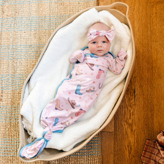 Baby wrapped in a pink blanket with cowboy print in a wooden crib.