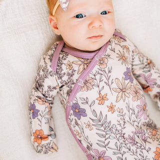 Baby wearing a floral onesie with purple accents on a white background