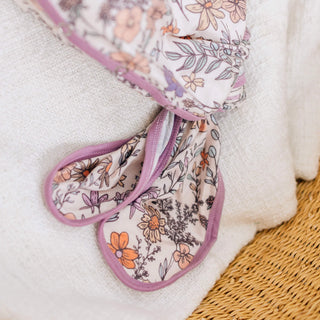 Floral-patterned oven mitts with a white towel and woven surface in the background