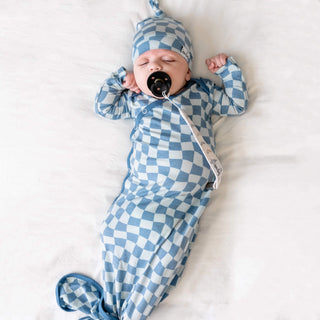Baby in blue checkered outfit and hat lying on a white surface