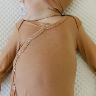 Brown baby onesie with buttons on a textured surface