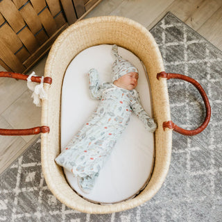 Newborn baby in a Moses basket with a patterned outfit and hat on a wooden floor.