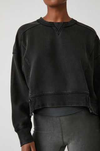 A cropped black sweatshirt with a washed, faded texture, worn by a model with gray ribbed leggings against a light gray studio background.