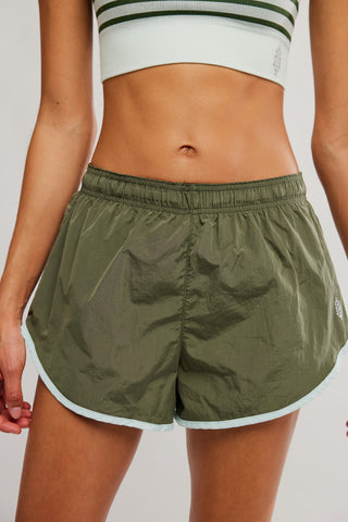 Person wearing green athletic shorts and a white crop top with green stripes on a light gray background