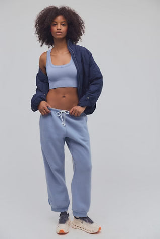 A model wearing a light blue crop top, matching sweatpants with a white drawstring, a navy blue open jacket, and sneakers, standing against a light gray studio background.