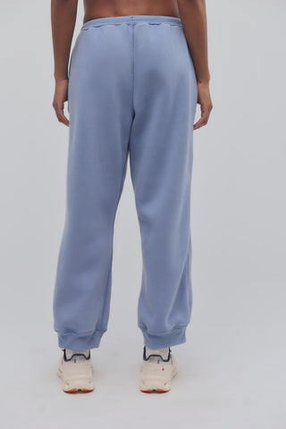 A person shown from the back wearing light blue sweatpants and cream sneakers against a plain light gray studio background.