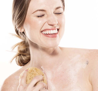 Woman applying body wash with a sponge applicator on a white background