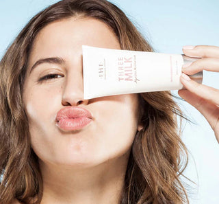 Woman holding a skincare product labeled 'Three Milk' against a light blue background