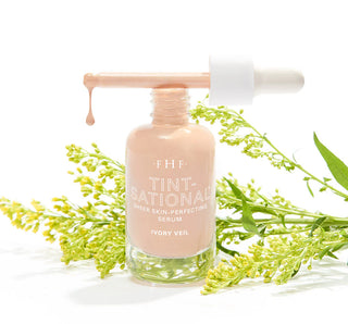 Serum bottle with dropper labeled 'Tint-Sational' surrounded by green leaves on a white background