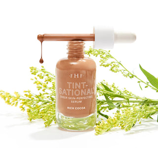 Serum bottle with dropper labeled 'FHF Tint-National' surrounded by green leaves on a white background