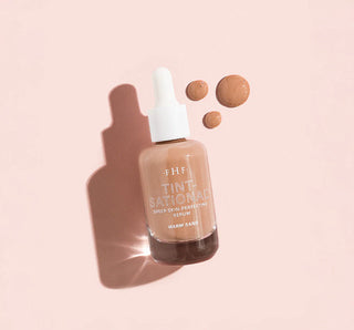 Bottle of FHF Tint National serum with droplets on a pink background