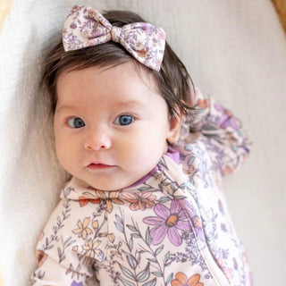 Baby wearing a floral outfit and headband with a neutral background