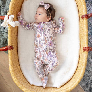 Baby in a floral onesie lying in a moses basket with white bedding.